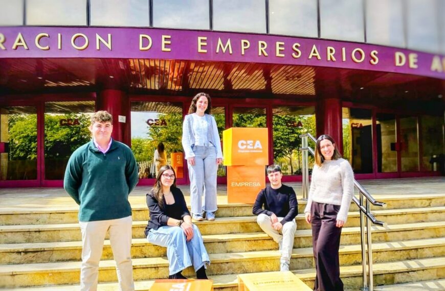 Cinco jóvenes estudiantes posan sonrientes en la escalinata de entrada de la sede de la Confederación de Empresarios de Andalucía (CEA). Se trata de Ander Aragón, María Vázquez, Rosa Fernández, Antonio Jesús Orellana y María Fernández, quienes se incorporan a distintos departamentos de la organización para realizar su formación práctica. En la imagen, los alumnos aparecen rodeados de cubos naranjas decorativos con el logotipo de la CEA y el lema "Andalucía y sus empresas. Generando confianza", bajo el rótulo principal del edificio de la patronal andaluza.