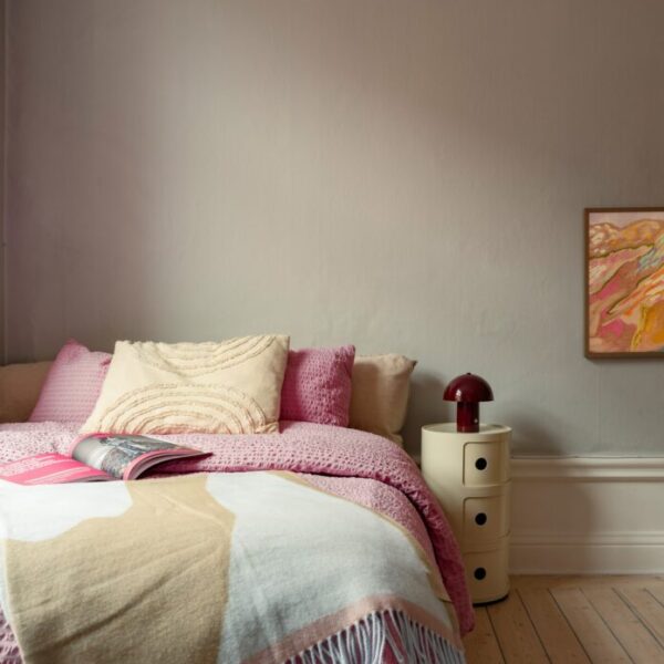 Dormitorio nórdico con cama colorida en rosa y colcha de gofre, estanterías de madera y lámina de Picasso en Estocolmo