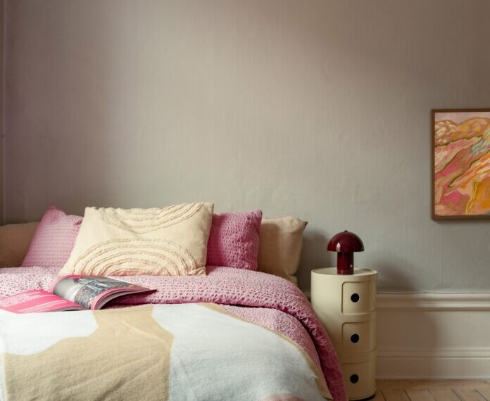 Dormitorio nórdico con cama colorida en rosa y colcha de gofre, estanterías de madera y lámina de Picasso en Estocolmo